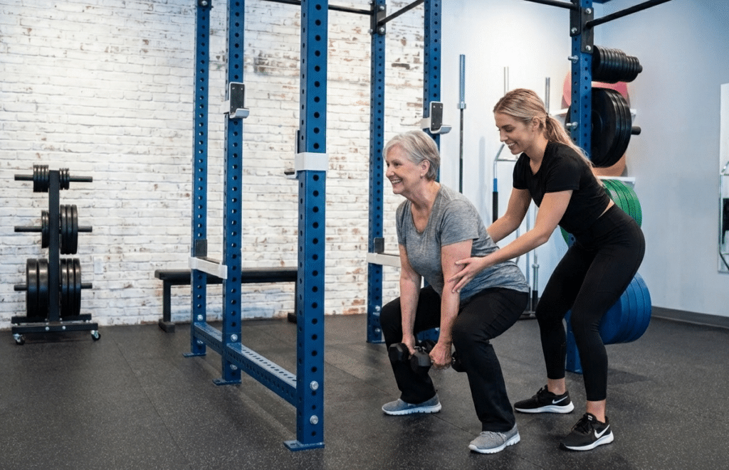 Personal trainer helping senior woman perform supervised strength training for bone health